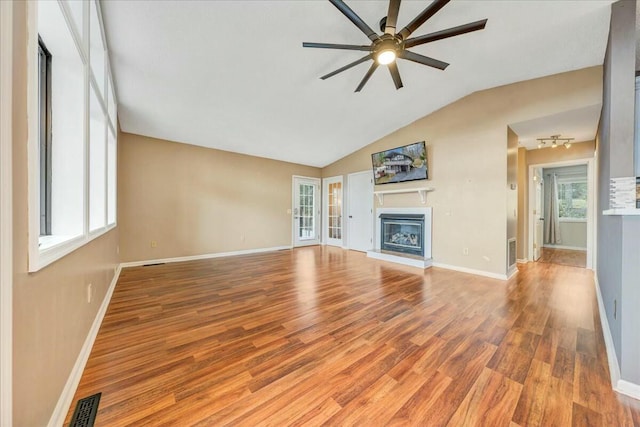 unfurnished living room with wood finished floors, visible vents, baseboards, a ceiling fan, and a glass covered fireplace