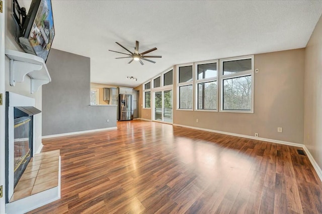 unfurnished living room featuring a healthy amount of sunlight, ceiling fan, wood finished floors, and a glass covered fireplace