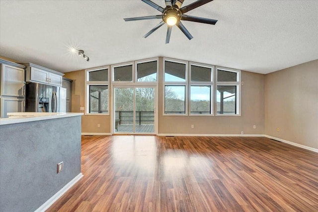 unfurnished living room featuring dark wood-type flooring, a ceiling fan, and baseboards