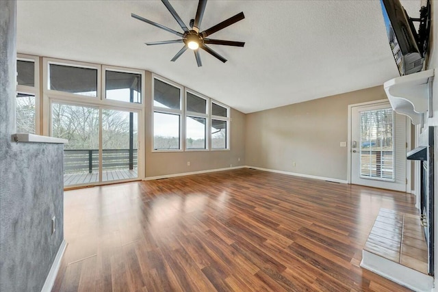 unfurnished living room with baseboards, dark wood finished floors, a ceiling fan, lofted ceiling, and a textured ceiling