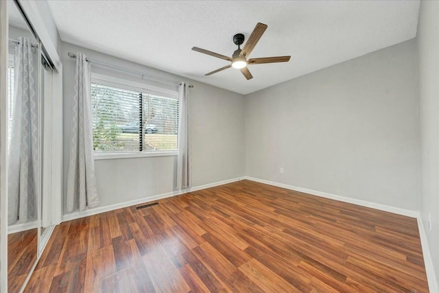 unfurnished room with ceiling fan, a textured ceiling, wood finished floors, visible vents, and baseboards