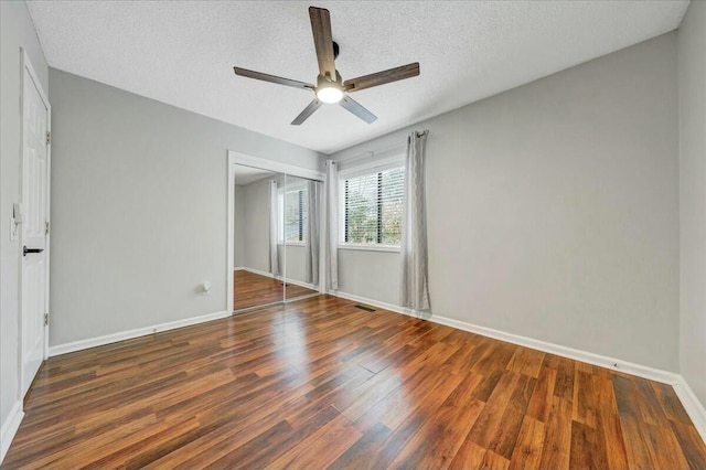 unfurnished bedroom with dark wood-style floors, a closet, visible vents, a textured ceiling, and baseboards