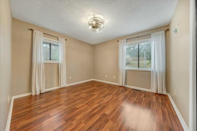 unfurnished room with visible vents, plenty of natural light, baseboards, and wood finished floors