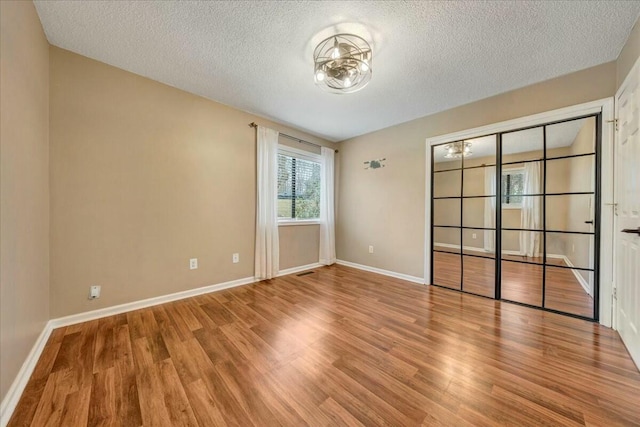 spare room with a textured ceiling, light wood-type flooring, visible vents, and baseboards