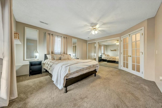 bedroom with light carpet, french doors, a textured ceiling, and two closets