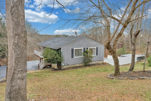 view of side of property featuring roof with shingles, a lawn, stairway, and fence