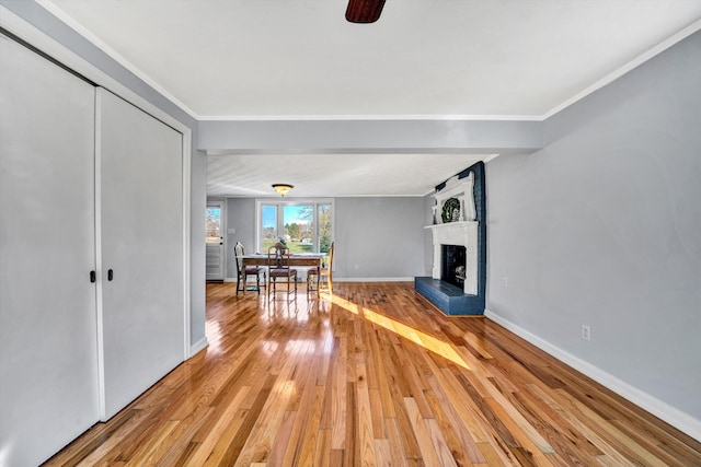 unfurnished living room with light wood-type flooring, a brick fireplace, ceiling fan, and crown molding