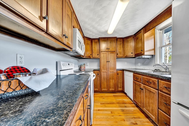 kitchen with white appliances, light hardwood / wood-style flooring, dark stone counters, and sink