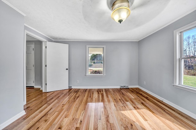 spare room with crown molding, a healthy amount of sunlight, a textured ceiling, and light wood-type flooring