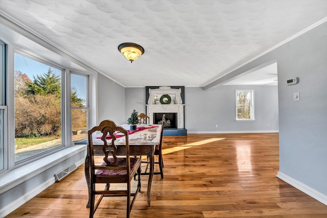dining room with a large fireplace, wood-type flooring, and ornamental molding