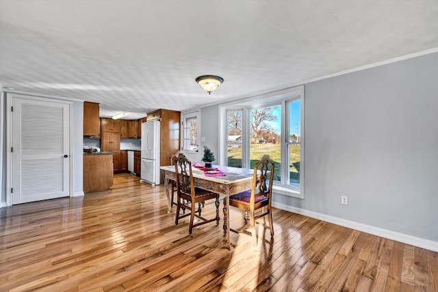 dining space with ornamental molding and light hardwood / wood-style flooring