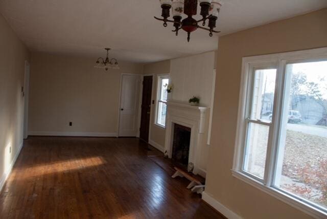 unfurnished living room featuring a healthy amount of sunlight, dark hardwood / wood-style flooring, and a chandelier