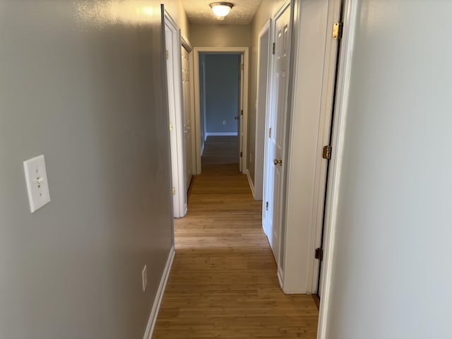 hall with a textured ceiling and light hardwood / wood-style floors