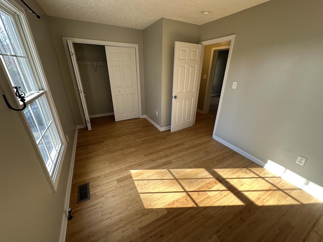 unfurnished bedroom featuring light hardwood / wood-style flooring, multiple windows, and a closet