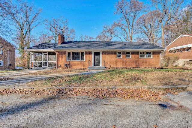 ranch-style home featuring driveway, brick siding, a chimney, and a sunroom