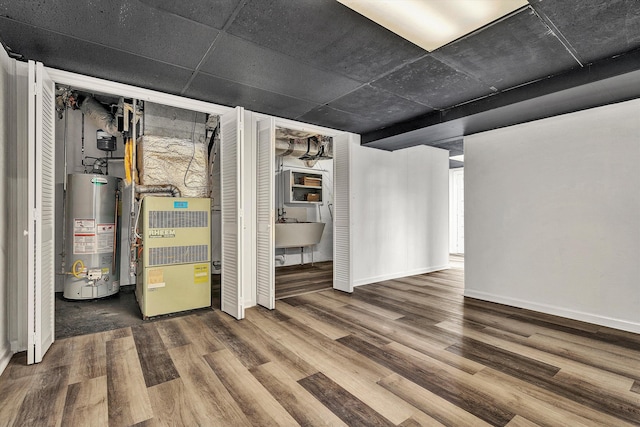 finished basement featuring a sink, gas water heater, wood finished floors, and baseboards