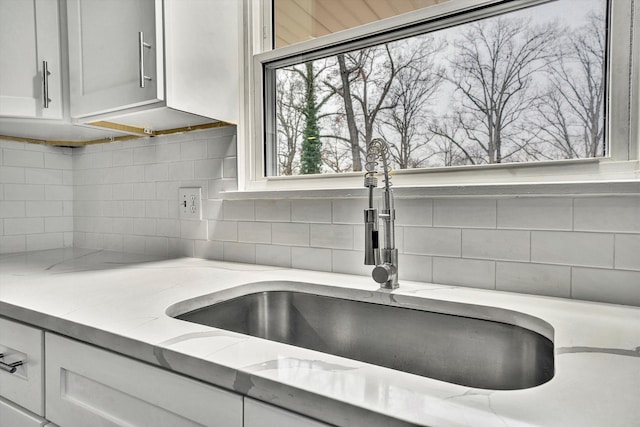 room details featuring tasteful backsplash, white cabinetry, a sink, and light stone countertops