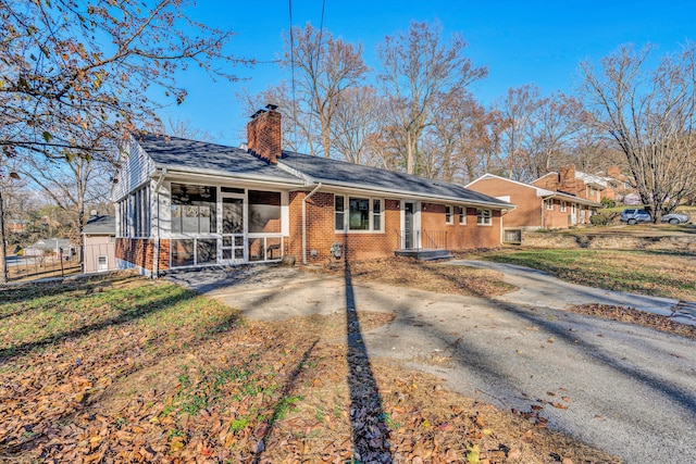 ranch-style house with driveway, brick siding, a chimney, and a sunroom