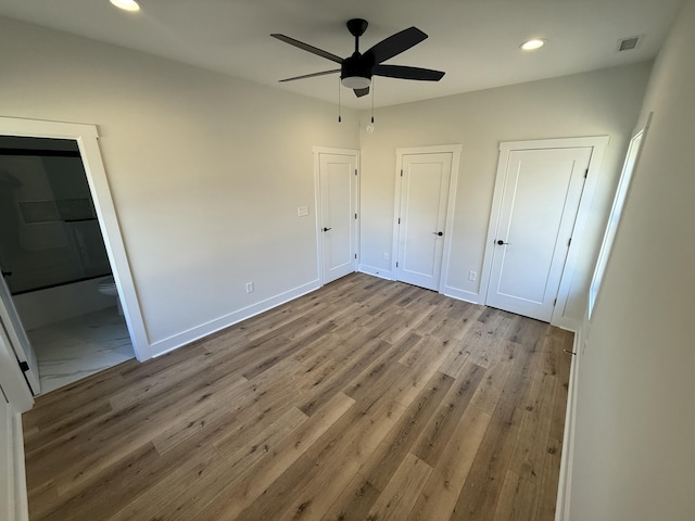 unfurnished bedroom featuring connected bathroom, ceiling fan, light hardwood / wood-style flooring, and two closets