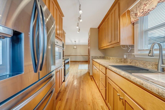 kitchen with appliances with stainless steel finishes, track lighting, sink, light hardwood / wood-style floors, and hanging light fixtures