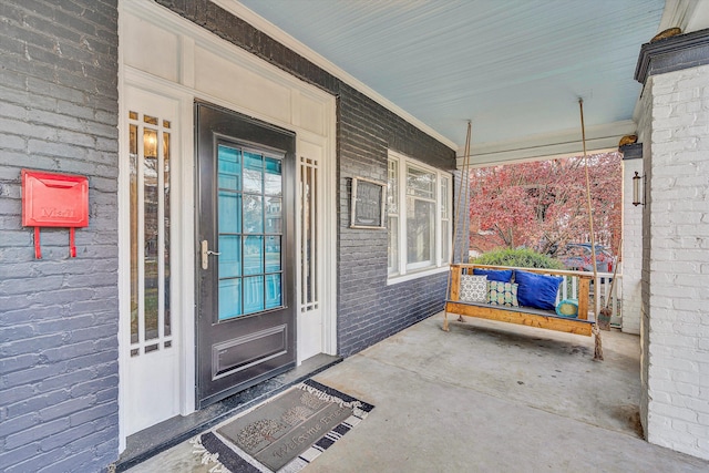 view of exterior entry featuring a porch and brick siding