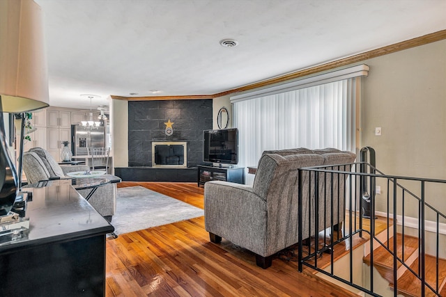 living room with a tiled fireplace, hardwood / wood-style flooring, crown molding, and an inviting chandelier