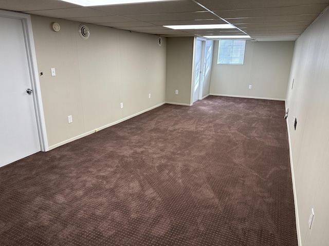 basement with a paneled ceiling and dark carpet