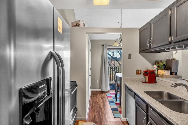 kitchen with sink, dark wood-type flooring, stainless steel appliances, light stone counters, and dark brown cabinets