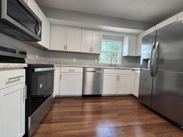 kitchen with sink, appliances with stainless steel finishes, white cabinetry, dark hardwood / wood-style floors, and light stone counters