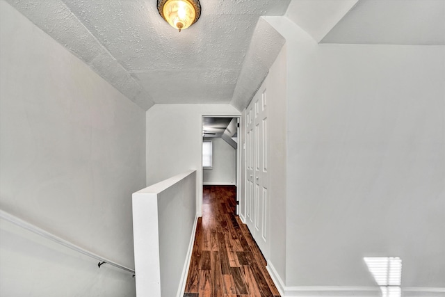 corridor featuring a textured ceiling, dark hardwood / wood-style floors, and vaulted ceiling