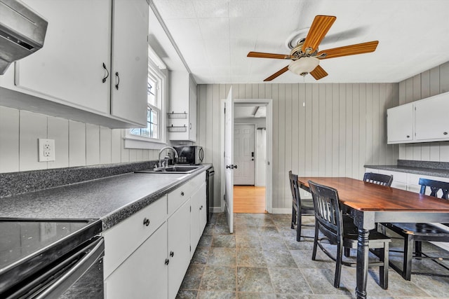 kitchen with ceiling fan, white cabinetry, sink, and wooden walls