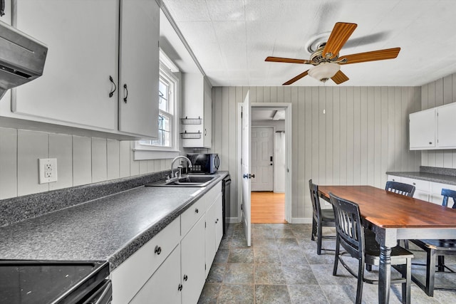 kitchen with ceiling fan, sink, white cabinets, and wood walls