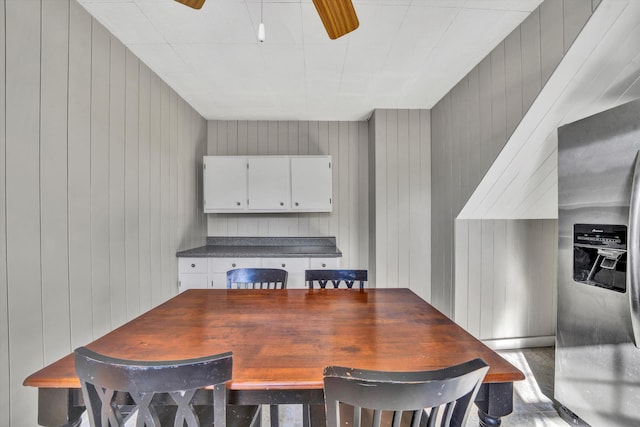 dining space with ceiling fan and wooden walls