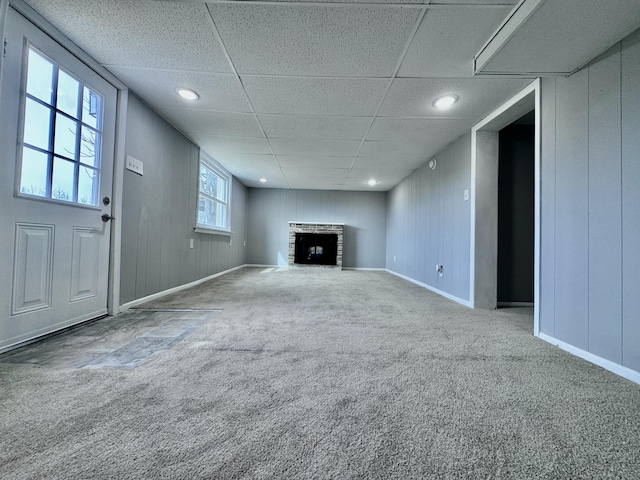 unfurnished living room with a drop ceiling, a fireplace, carpet flooring, and baseboards