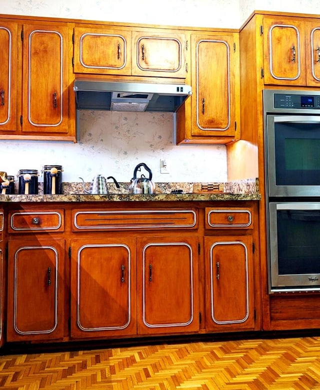 kitchen featuring decorative backsplash, stainless steel double oven, light parquet floors, and light stone counters