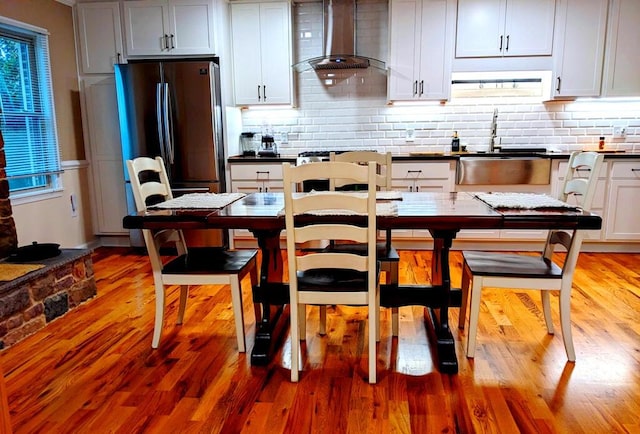 kitchen featuring stainless steel refrigerator, sink, wall chimney exhaust hood, wood-type flooring, and white cabinets