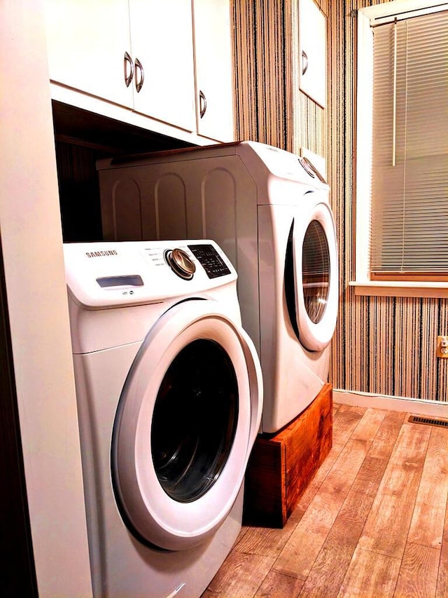 laundry area featuring washer and dryer, light hardwood / wood-style floors, and cabinets