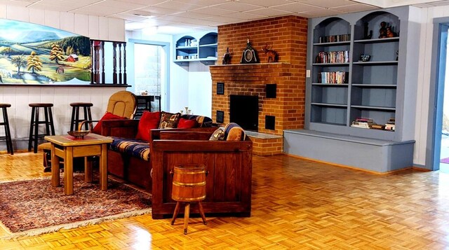 living room with a fireplace, built in shelves, light parquet floors, and a drop ceiling