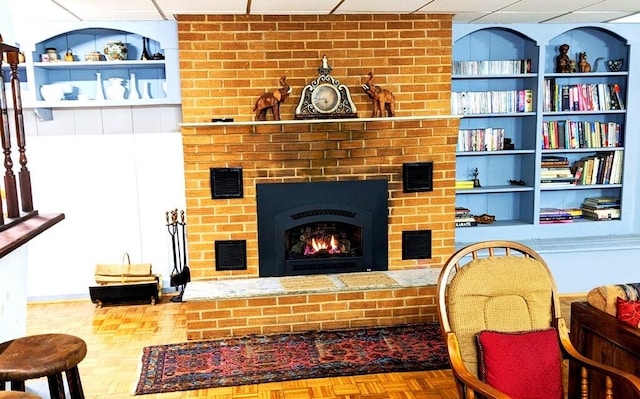 living room with a brick fireplace, a paneled ceiling, built in features, and parquet floors