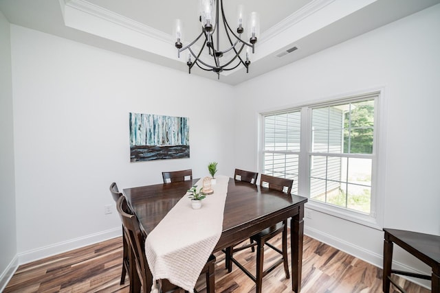 dining space featuring a raised ceiling, crown molding, wood-type flooring, and a notable chandelier