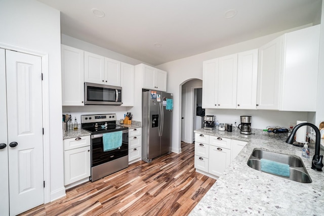 kitchen with white cabinets, sink, light wood-type flooring, light stone counters, and stainless steel appliances