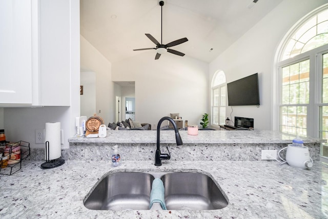 kitchen with high vaulted ceiling, sink, ceiling fan, light stone countertops, and white cabinetry