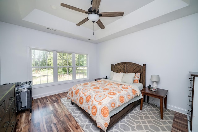 bedroom with a raised ceiling, ceiling fan, and dark wood-type flooring