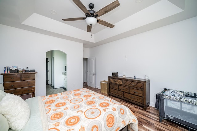 bedroom featuring hardwood / wood-style flooring, ceiling fan, connected bathroom, and a tray ceiling