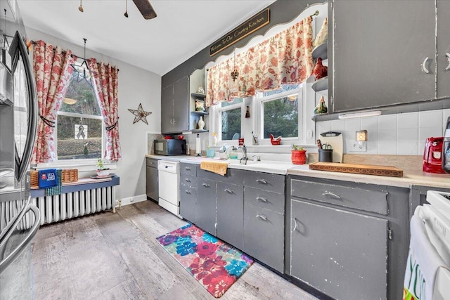 kitchen featuring backsplash, gray cabinetry, white dishwasher, ceiling fan, and hardwood / wood-style flooring