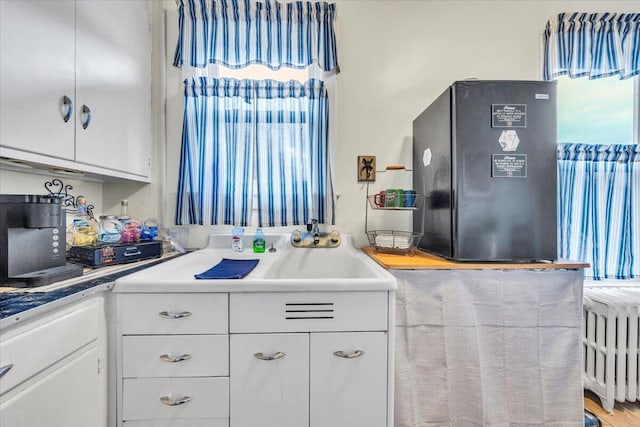 kitchen with black refrigerator, white cabinetry, radiator heating unit, and hardwood / wood-style floors