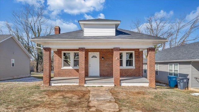 bungalow with a porch, brick siding, a chimney, and a front lawn