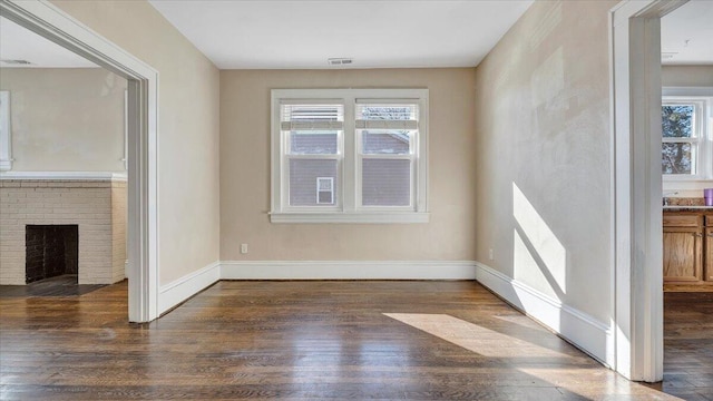 interior space with a brick fireplace, a healthy amount of sunlight, dark wood finished floors, and baseboards