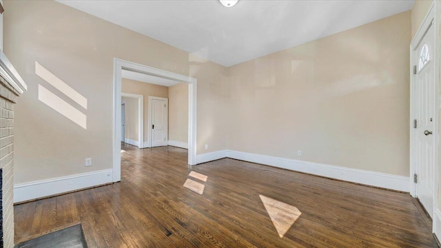 spare room featuring dark wood-type flooring, a fireplace, and baseboards