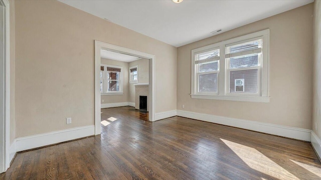 unfurnished room with dark wood-type flooring, visible vents, plenty of natural light, and baseboards